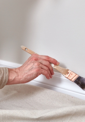 Artisan appliquant une peinture blanche au pinceau sur une plinthe murale