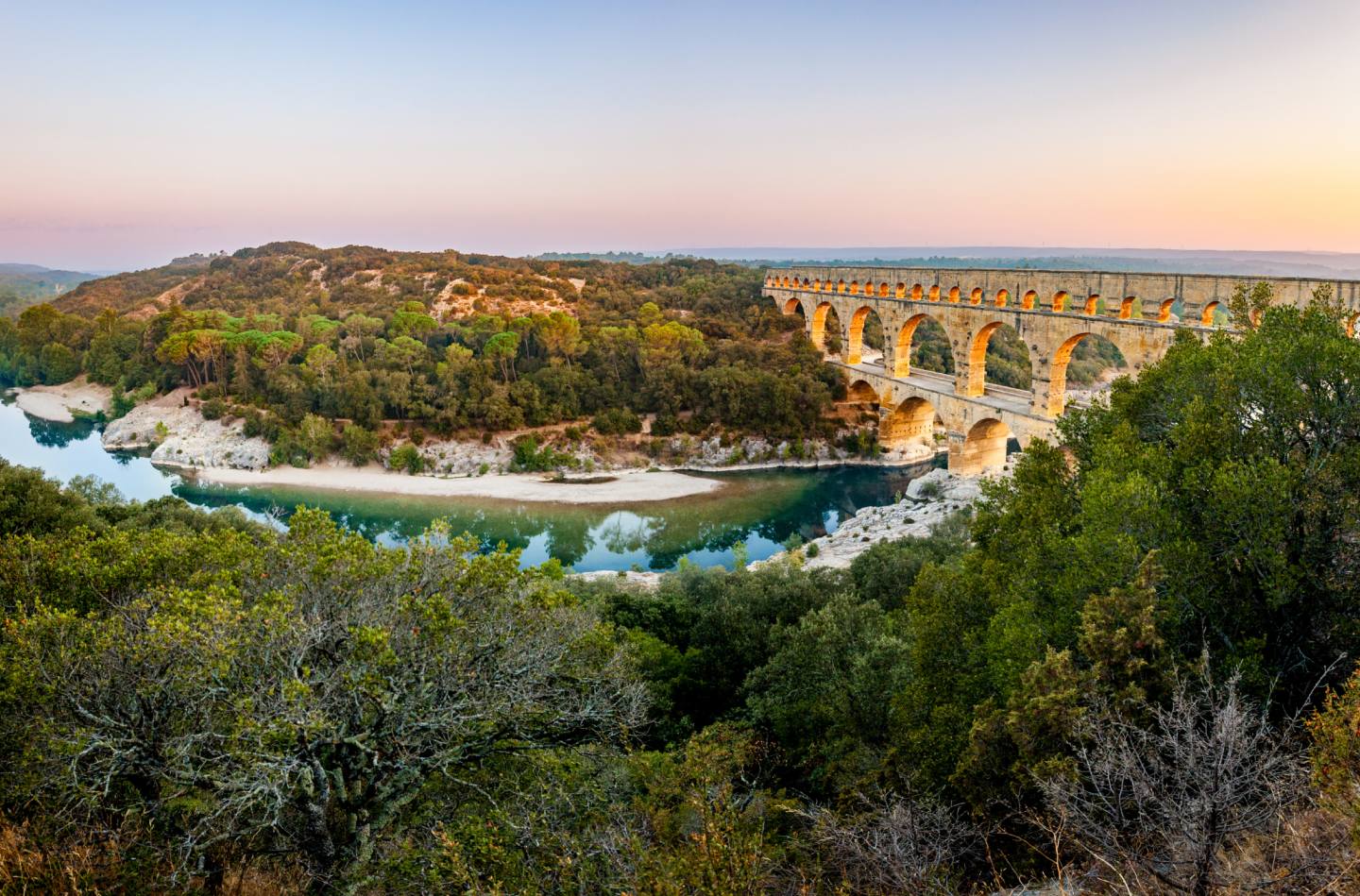 Pont du Gard au coucher du soleil avec ses arches en pierre au-dessus d’une rivière entourée de verdure
